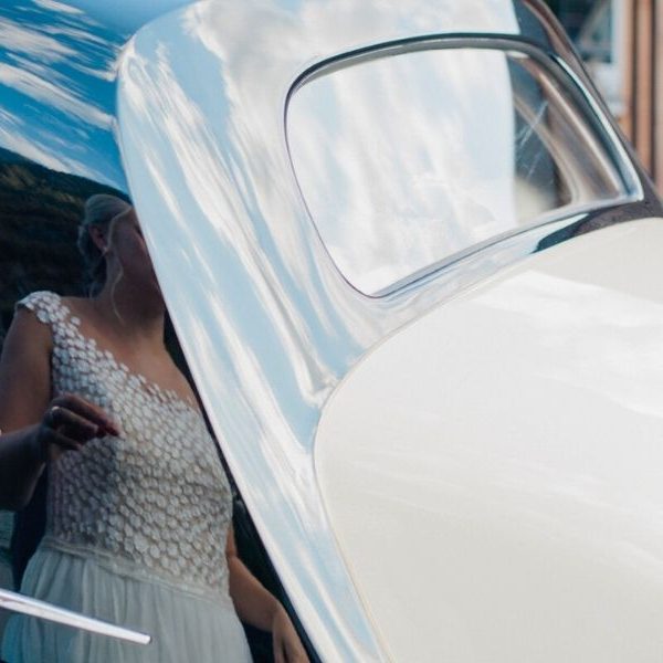 Une femme en robe de mariée qui ouvre la portière d'une voiture de collection